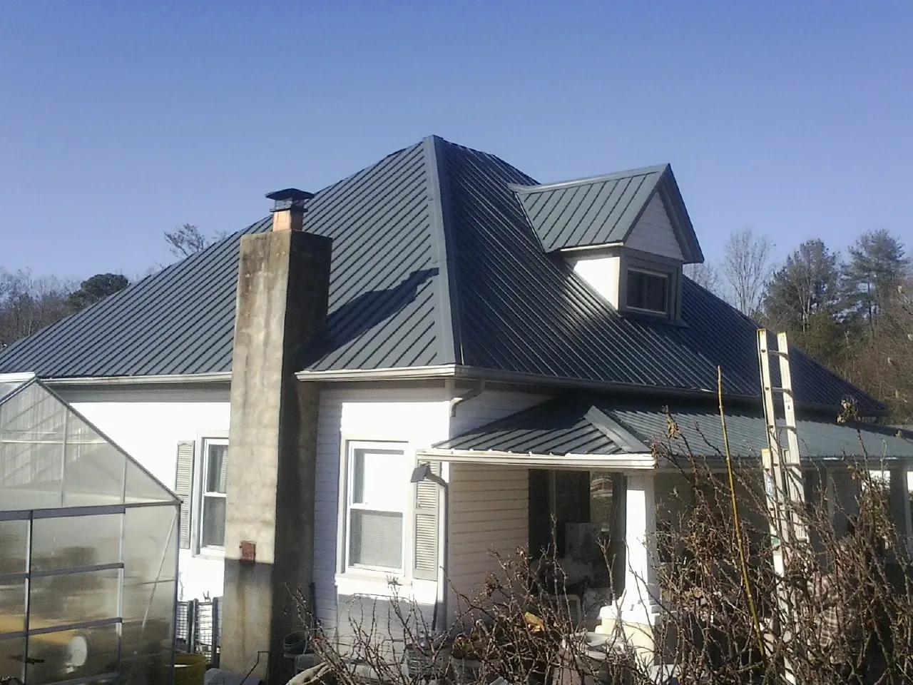 Dark blue standing seam metal roof on a white farmhouse with dormer — Slate & Tile Roof Repair by Roofing Brothers in Percival
