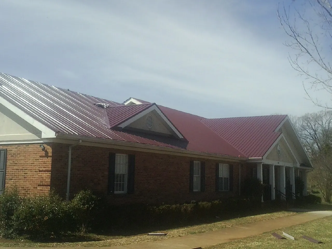 Red metal roof with gabled entries on a long brick building, from a Hail Damage Roof Repair job in Percival