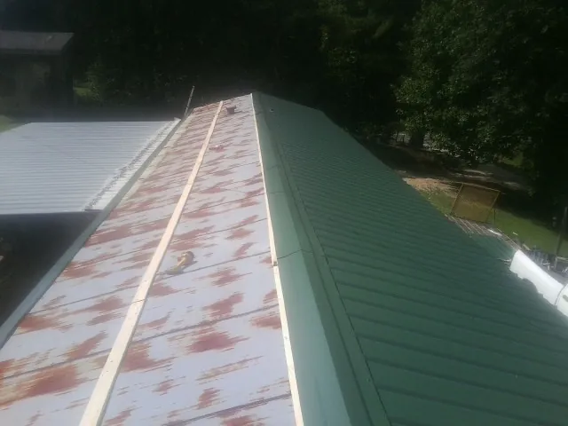 Old rusted panels beside newly installed green metal roofing — Wind Damage Roof Repair by Roofing Brothers in Percival