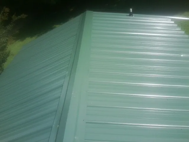 New green metal panels meeting at the ridge of a roof — Flat Roof Repair work by our crew in Percival