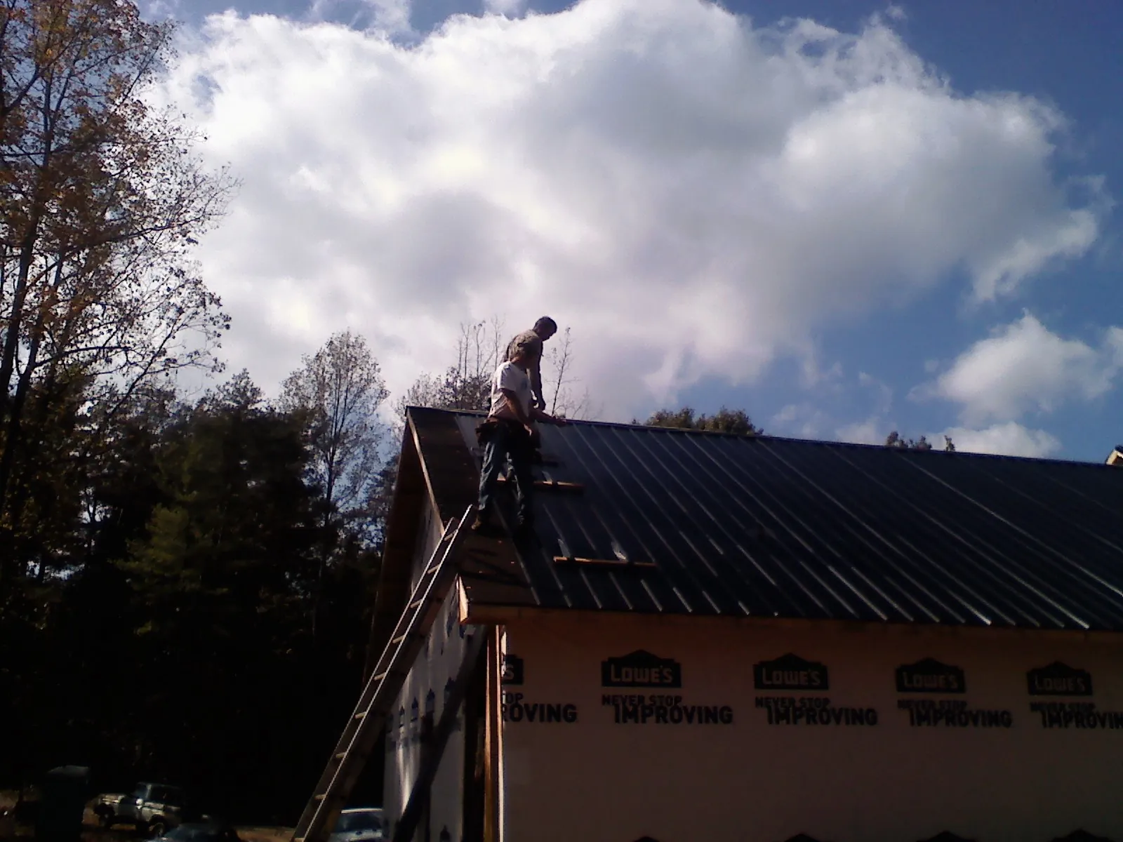 Roofer fastening dark metal panels high against a cloudy sky, from a Roof Inspection job in Percival