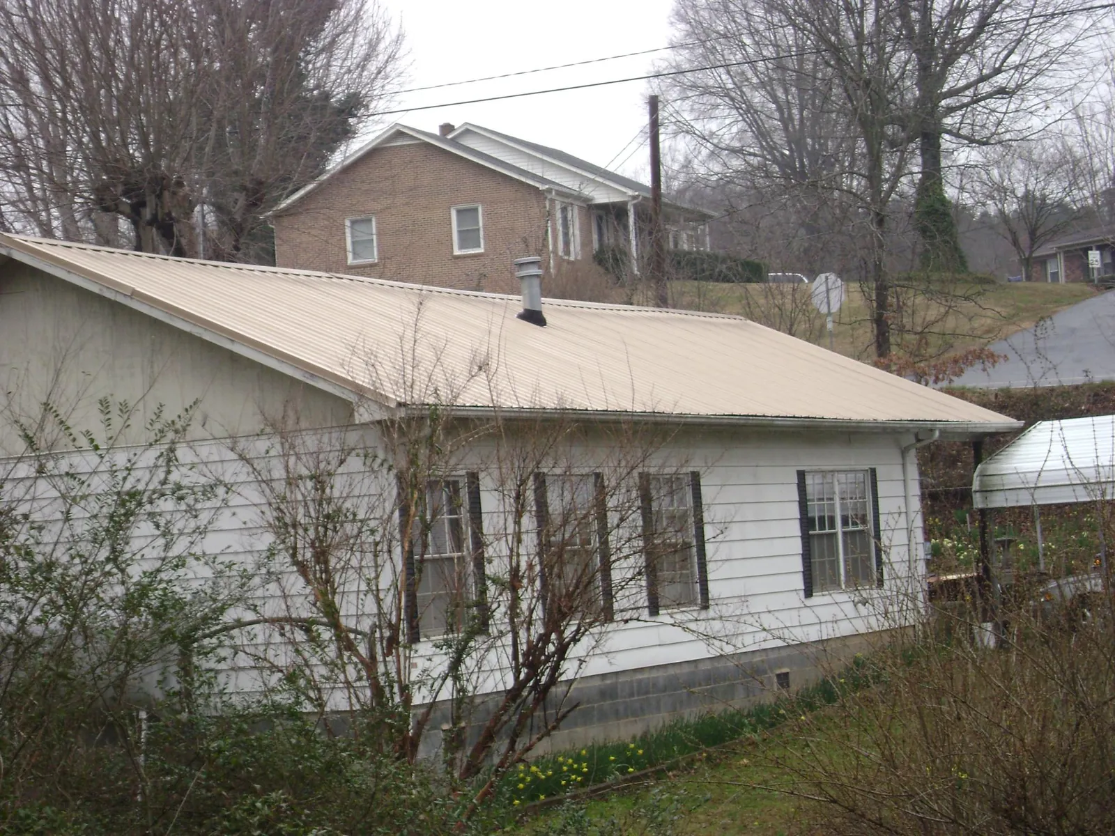 Tan metal roof on a white sided house set into a hillside — Commercial Roofing by Roofing Brothers in Percival